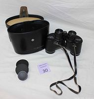 Vintage Bushnell Sportview 7x35 binoculars alongside original black carrying case and three lens caps on a white surface.