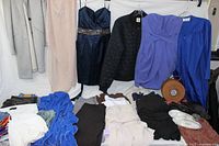 Photo of dresses, tops, pants, shoes, and accessories laid out and hung on a white sheet background.