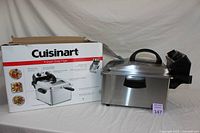Photo of the Cuisinart deep fryer next to its original box showing front and side view of the stainless steel unit with black handle and control panel attached.
