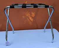 Folding chrome luggage rack standing upright showing side angle with black straps and chrome frame.