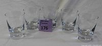 Five clear glass highball glasses arranged in a row with a small purple auction marker in front.