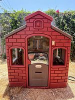 Front view of the Little Tikes playhouse showing red brick patterned wall with door and window openings.