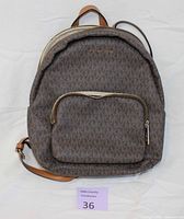 Front view of Michael Kors Erin backpack with brown MK logo print, zip front pocket, and adjustable brown leather straps laid flat.