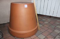 Side view of one large terracotta ceramic pot with a ruler showing height measurement on a brick patio.