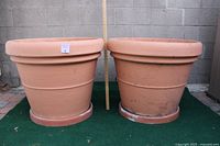 Two oversized plastic pots side by side against a cinder block wall with a measuring stick showing height.