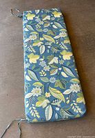 Cushion folded showing floral design, ties at corners, laid on floor.