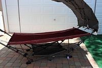 Full view of the portable free-standing hammock with maroon fabric and black metal frame stand.