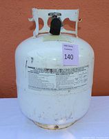 Front view of white propane tank showing safety warning labels and some wear marks.