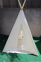 Full view of white cloth covered teepee showing triangular entrance and wooden poles at base.