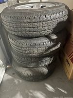 Stack of four used Jeep tires mounted on silver aluminum rims, showing tread condition and general appearance.