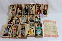 16 boxed vintage Italian dolls dressed in traditional costumes arranged on a flat surface, with an informational sheet beside them.