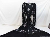 Full view of the black floor-length wrap-around dress laid out to show its length and pattern.