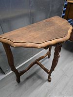 Front angled view of demilune table showing scalloped top, carved legs, stretcher