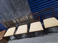 Four mid-century style wood dining chairs aligned side by side