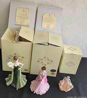Three Coalport figurines with their original boxes and information cards on display. The collectible figurines vary in size and wear random writing on the bottoms. Visual confirmation of included items to detail seller's description.