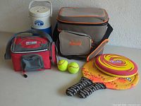Full view of the lot showing cooler bags, jug, tennis balls, paddles and frisbee