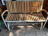 Full view of vintage garden glider swing showing the white metal frame and wooden slat seating and backrest placed indoors.