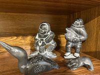 Four Inuit soapstone carvings arranged on wooden shelf: two human figures, one bird, one seal