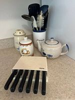 Full lot displayed on countertop showing ceramic teapot, ceramic garlic and mushroom holders, utensil holder with cooking utensils, and Wiltshire steak knife set