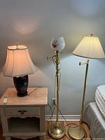 Two floor lamps standing by the wall and ceramic table lamp on nightstand, all lit up.