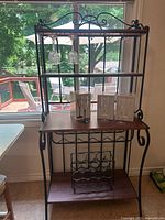 Full front view of metal bakers rack with wooden shelves, built-in wine rack, and 12 glass boxes on middle shelf, additional wine rack on bottom shelf.