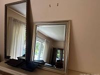 Two decorative mirrors at different sizes, shown standing on a flat surface with natural light reflection.