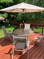 Full patio set showing hexagonal glass table, four chairs and umbrella on a deck with lawn background.