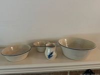 Photo showing three beige pottery bowls of different sizes with blue rims and one small white ceramic creamer with blue flower decoration.