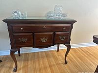 Front view of the colonial style side cabinet featuring four drawers, glass top, and cabriole legs.