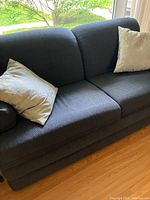 Front view of the blue upholstered sofa bed with two decorative light-colored throw pillows, showing the full seat and back cushions.
