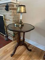 Side view of the mahogany pie crust table displaying the polished top with scalloped edges and the brass lamp on it.