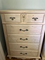Front view of the tall boy dresser showing five drawers with metal handles and floral painted designs on the top two drawers.