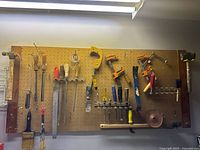 Photo of peg board with clamps, hand saws, screwdrivers, a coping saw, and a hand plane.