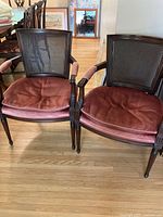 Front view of two Regency French cane armchairs with pink velvet cushions on seats and armrests, dark wood frames and cane backs.