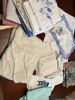 Folded linens with floral prints, lace, and scalloped edges placed on a table.