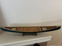 Side view of the wooden canoe model on the stand showing the dark green exterior and natural woodwork interior with seating visible.
