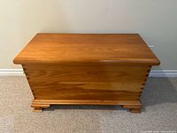 Front view of the wooden chest showing smooth flat top and dovetail corner joints, with bracket feet base on carpeted floor.