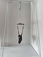 Assembled white metal stand with spring, chain, and black jumper seat harness suspended