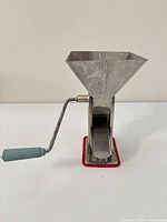 Metal hand-crank grinder front view, crank handle and hopper visible