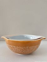 Side view of peach/orange Pyrex Woodland bowl stacked inside brown bowl