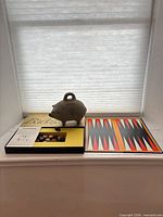 Backgammon set with board, box, rule sheet, pieces and stoneware piggy bank on windowsill