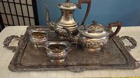 Full view of antique silver-plated tea service set on tray on table with blue wall background