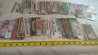 Photo showing various global banknotes laid out flat with measurement tape for scale.