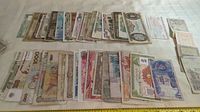 Photo showing an assortment of various global bank notes spread out on a table surface, multiple denominations and styles visible.