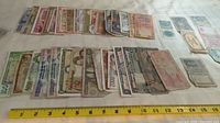 Photo showing assortment of approximately 40 banknotes of various denominations and origins, laid out horizontally with a measuring tape for scale.