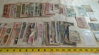 Overall layout photo showing about 40 assorted banknotes laid flat in rows on a white surface with a measuring tape for scale.