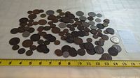 Wide view of a large assortment of Canadian pennies and other coins arranged on a white cloth beside a measuring tape.