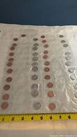 Coins arranged in rows inside plastic sleeves visible with measuring tape for scale.