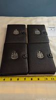 Four black leather coin cases with Canadian coat of arms emblem, arranged in two rows on a white surface with a measuring tape showing size.