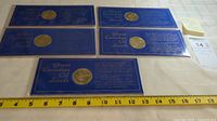 Five tokens mounted on blue display cards, arranged in two rows on a light surface with a measuring tape showing approximate width around 14 inches.